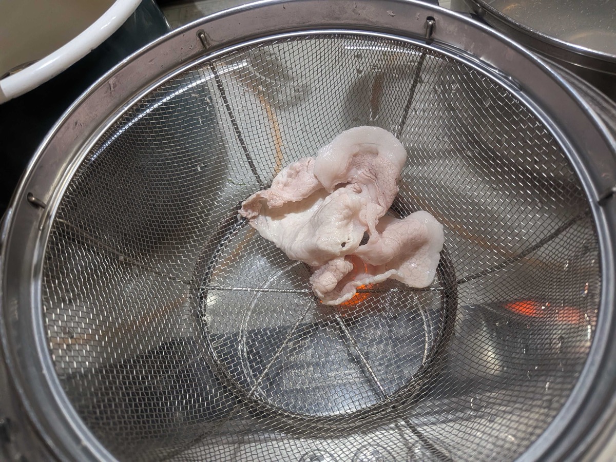 A poached slice of pork draining in a mesh strainer