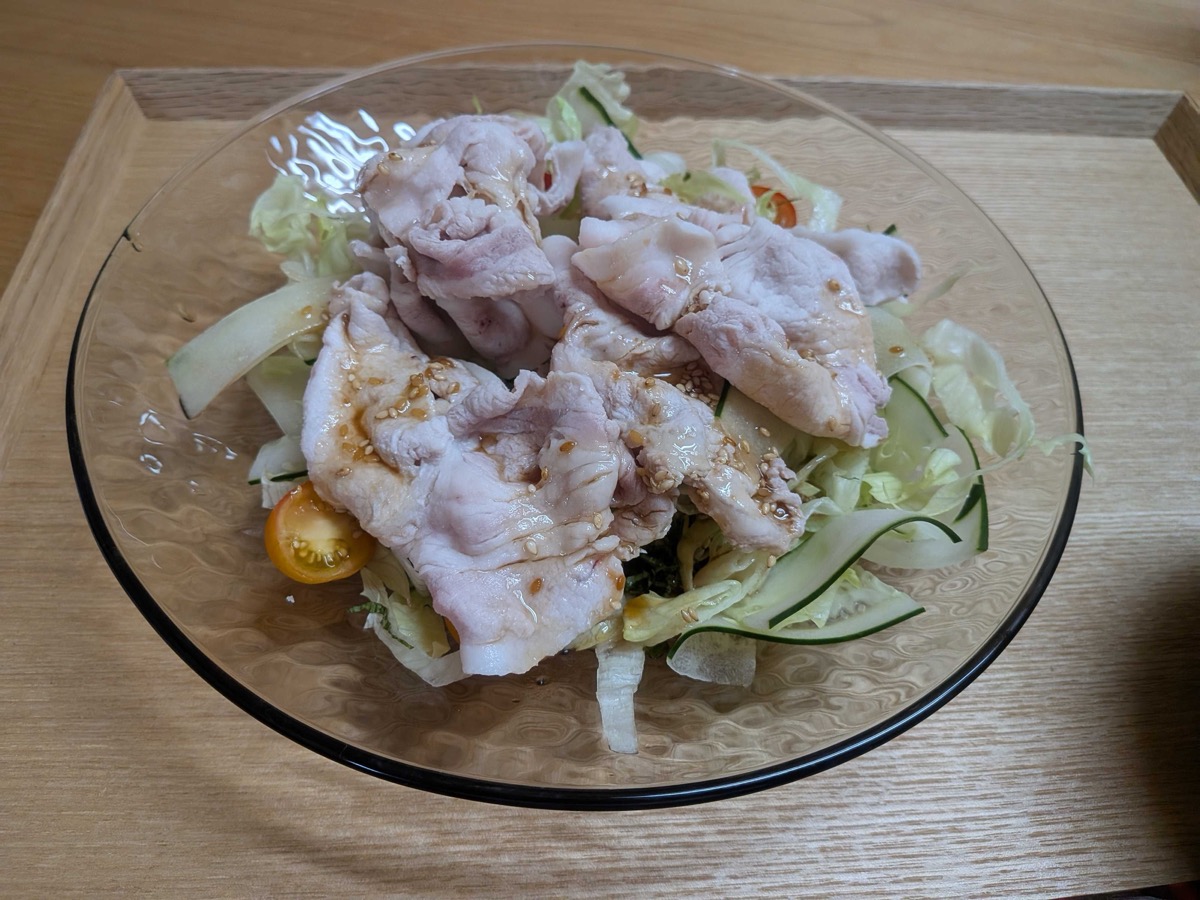 A glass plate of cold shabu-shabu salad — chilled poached pork over lettuce, cucumber, and cherry tomatoes with sesame dressing