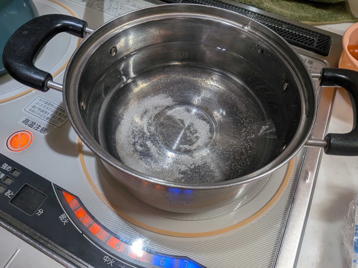 A pot of water heating on an induction cooktop for poaching the pork