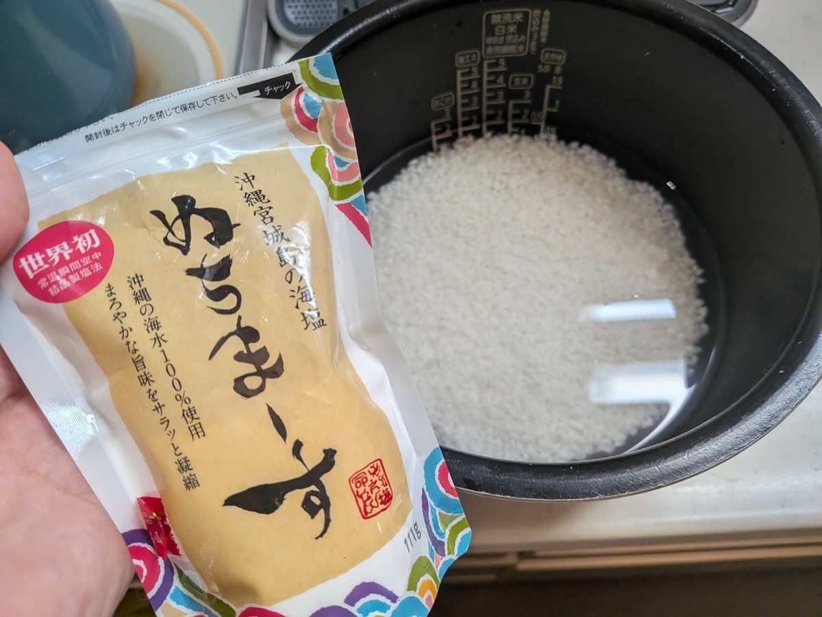 Adding Okinawan nuchima-su sea salt to soaked rice and water in the rice cooker pot