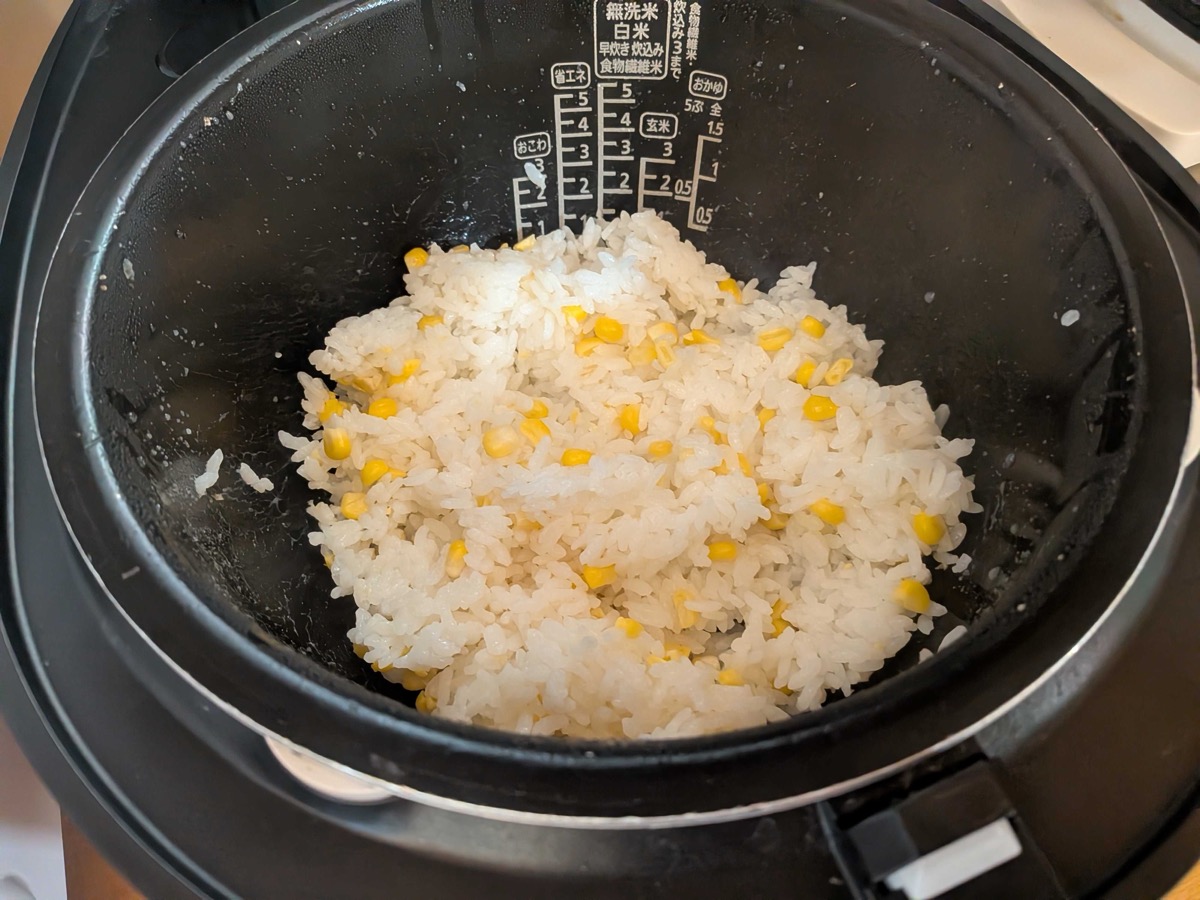 Freshly cooked corn rice in the rice cooker, white rice studded with golden corn kernels, being fluffed