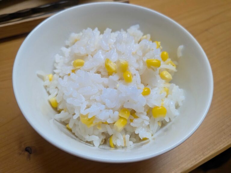 A white bowl of finished Japanese corn rice with golden kernels on a wooden table