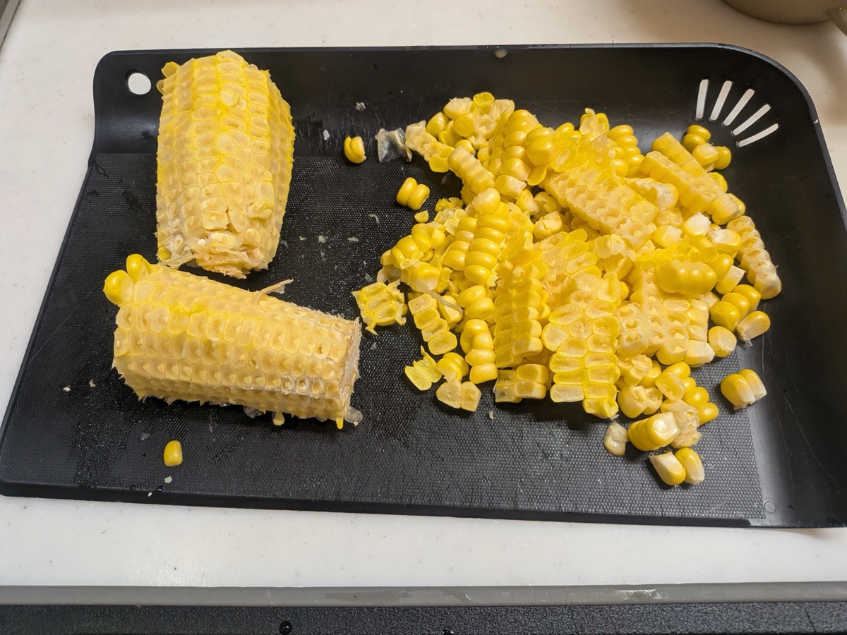 Fresh corn kernels cut off the cob piled on a black cutting board next to the stripped cobs
