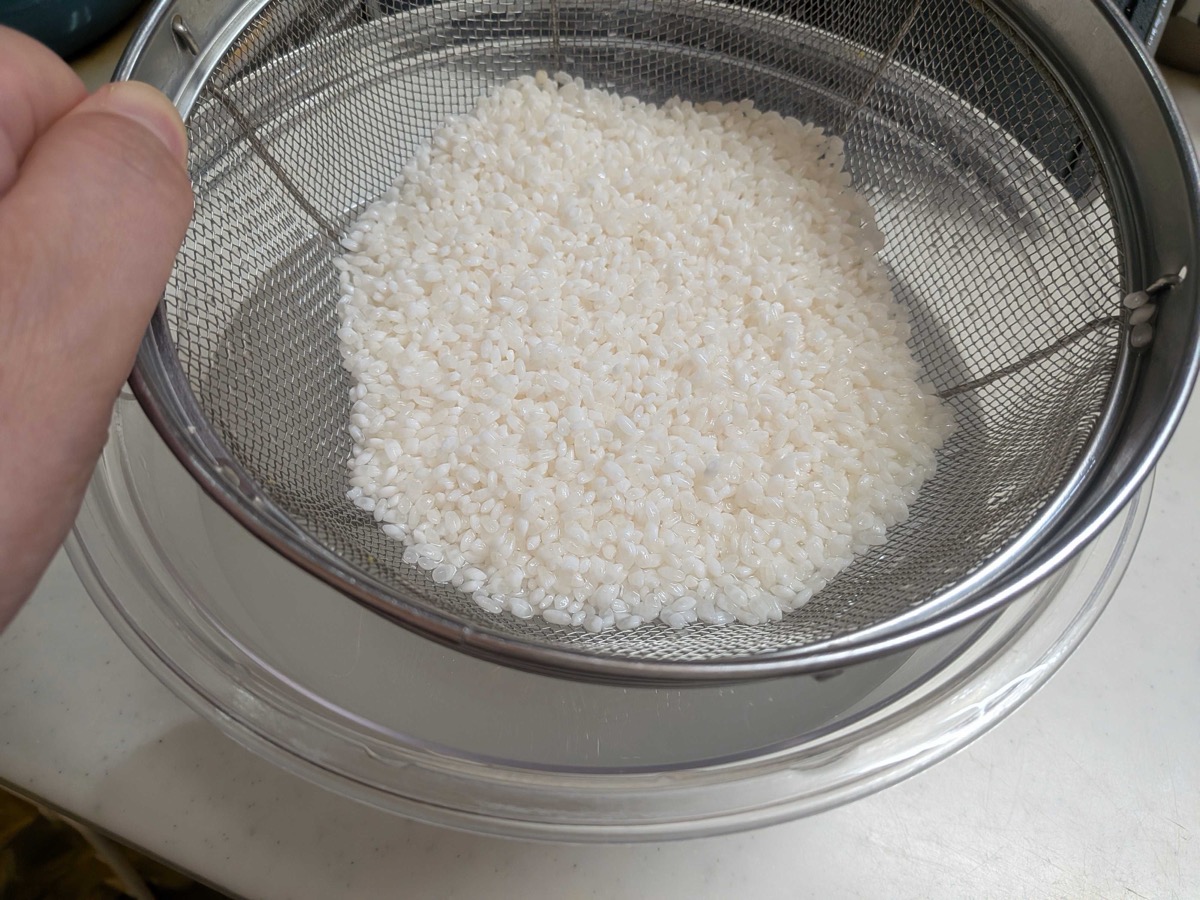 Rinsed white Japanese rice draining in a fine mesh sieve over a bowl