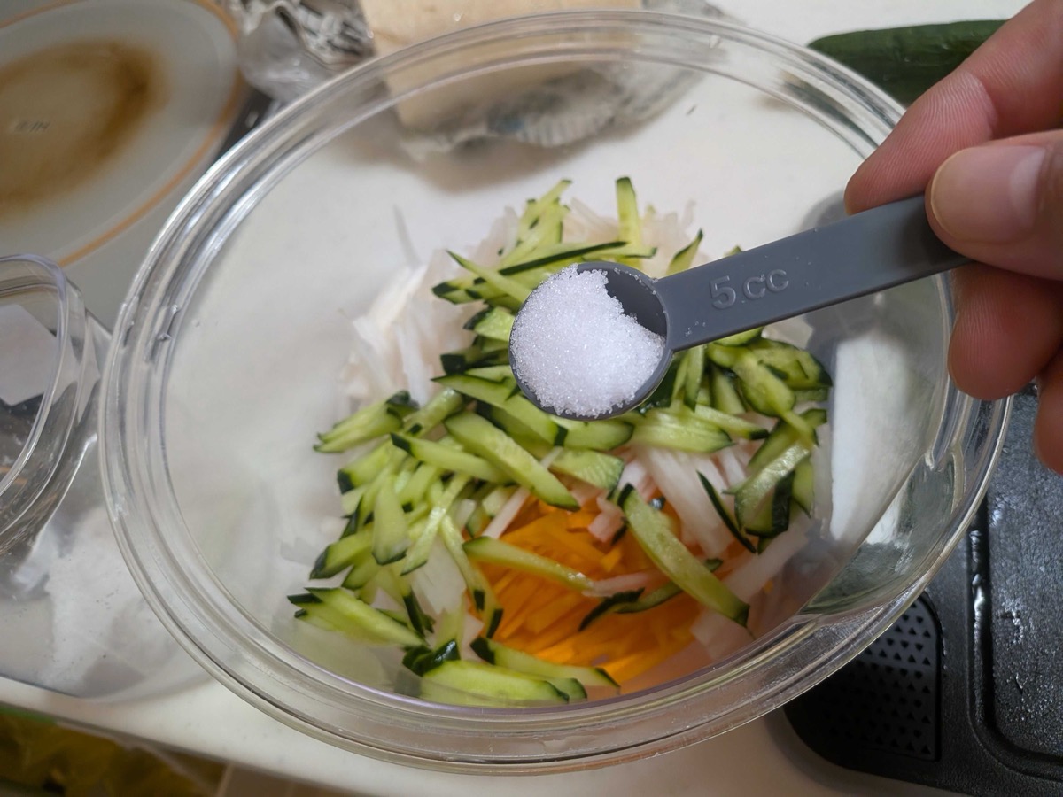A measuring spoon of salt being added to the shredded vegetables