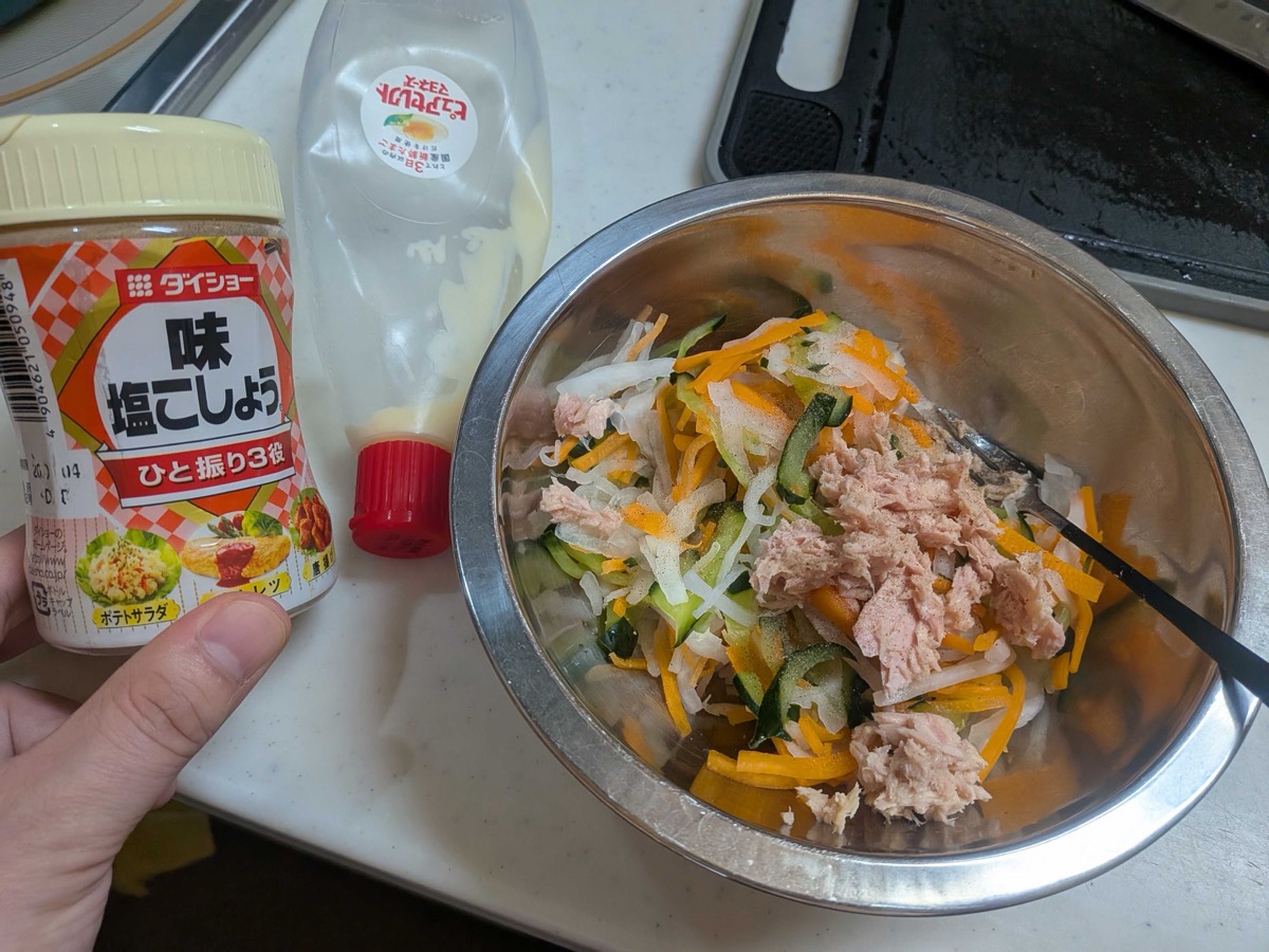 Tuna, salt and pepper, and mayonnaise being added to the vegetables in the bowl