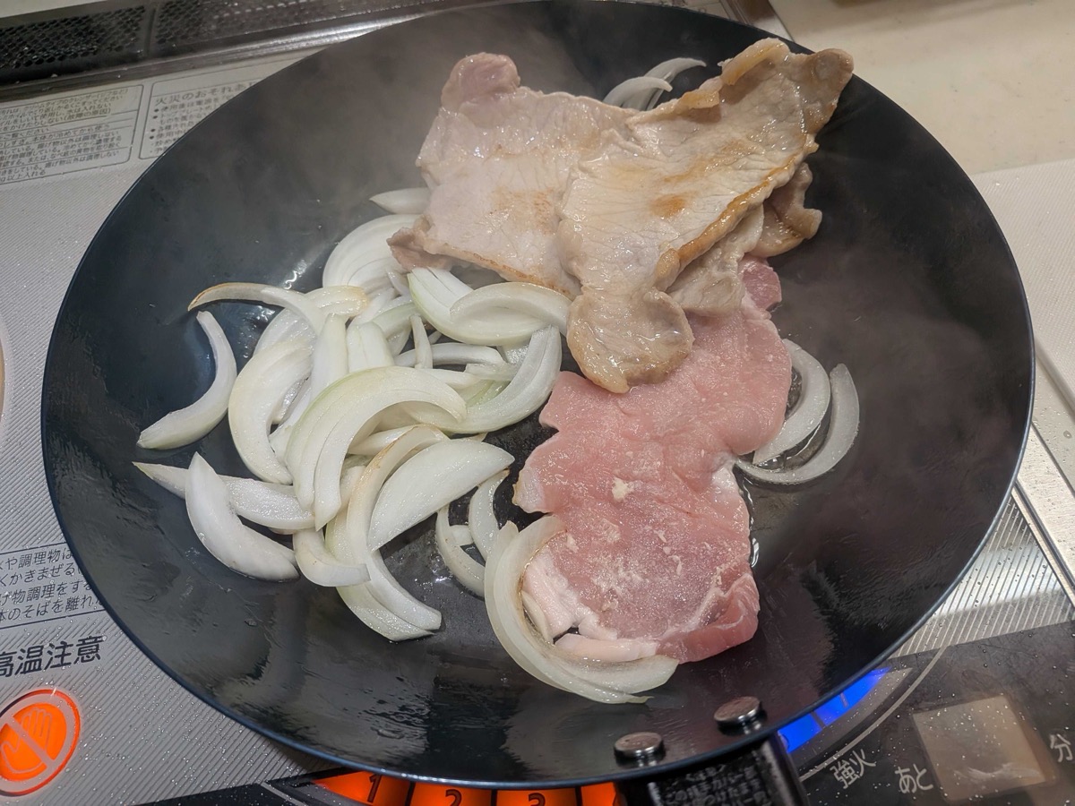 Sliced onion added to the pan alongside the frying pork