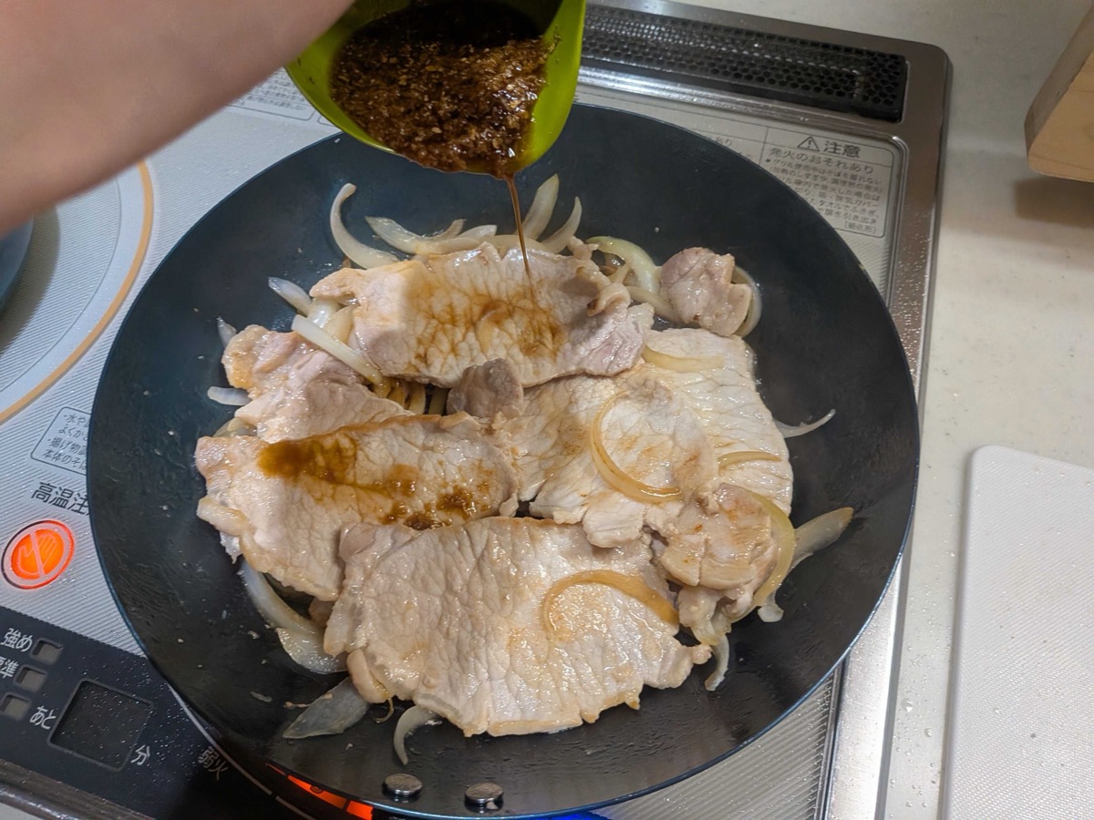 Ginger sauce being poured over the pork and onion in the pan