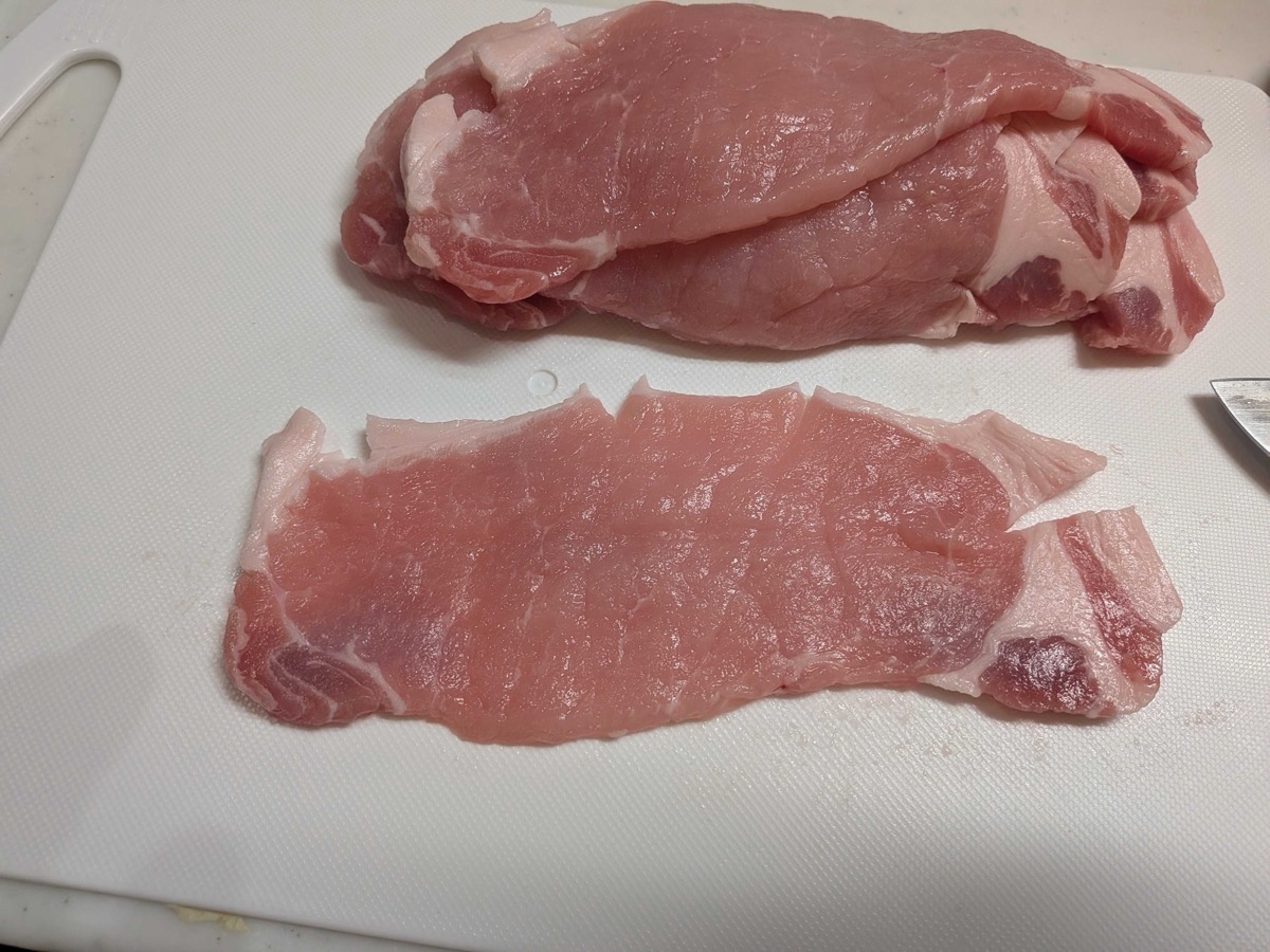 A thick pork loin steak butterflied open into a thin, wide piece on a cutting board
