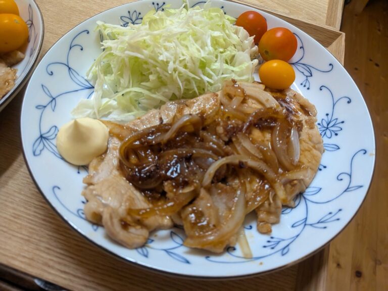 Japanese pork shogayaki with onion in ginger sauce, served with shredded cabbage, mayonnaise, and cherry tomatoes