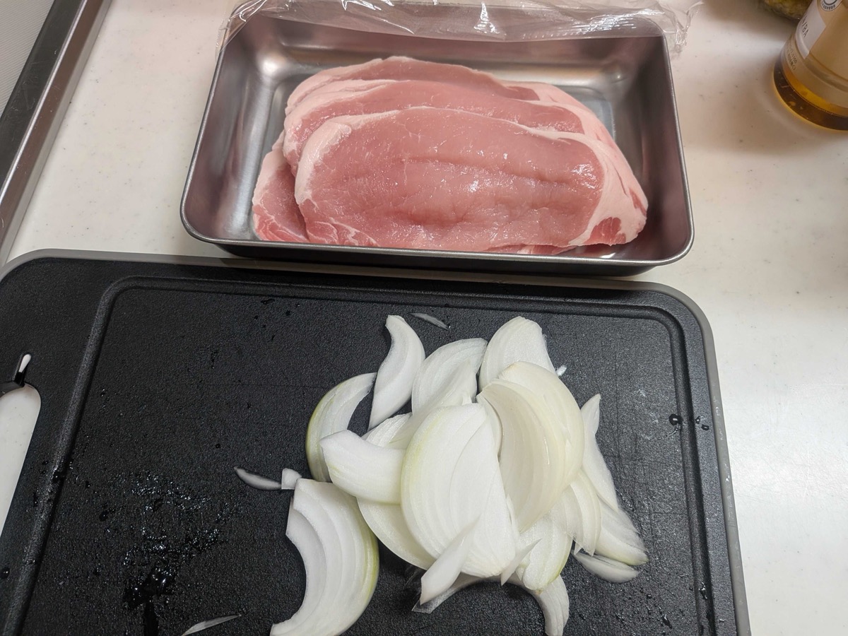 Thick-cut pork loin steaks in a metal tray next to sliced onion on a cutting board
