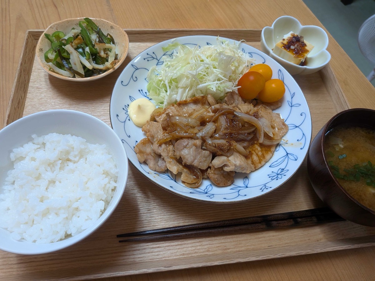 A full Japanese teishoku set — pork shogayaki, rice, miso soup, green pepper namul, and tofu on a wooden tray
