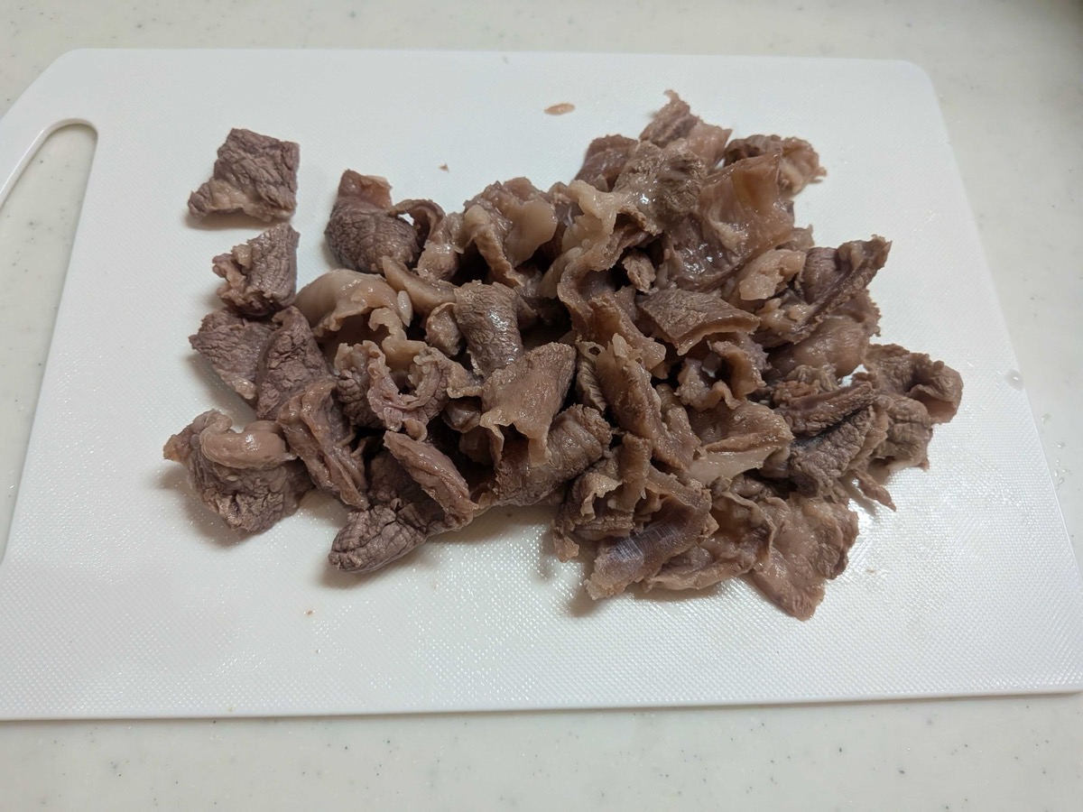 Pre-boiled beef sinew cut into bite-sized cubes on a white cutting board — pale brown and tender after the aku-nuki blanching step