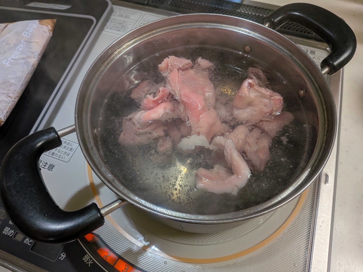 Raw beef sinew dropped into a pot of already-boiling water on an IH cooktop — the first blanching step for Japanese gyusuji nikomi