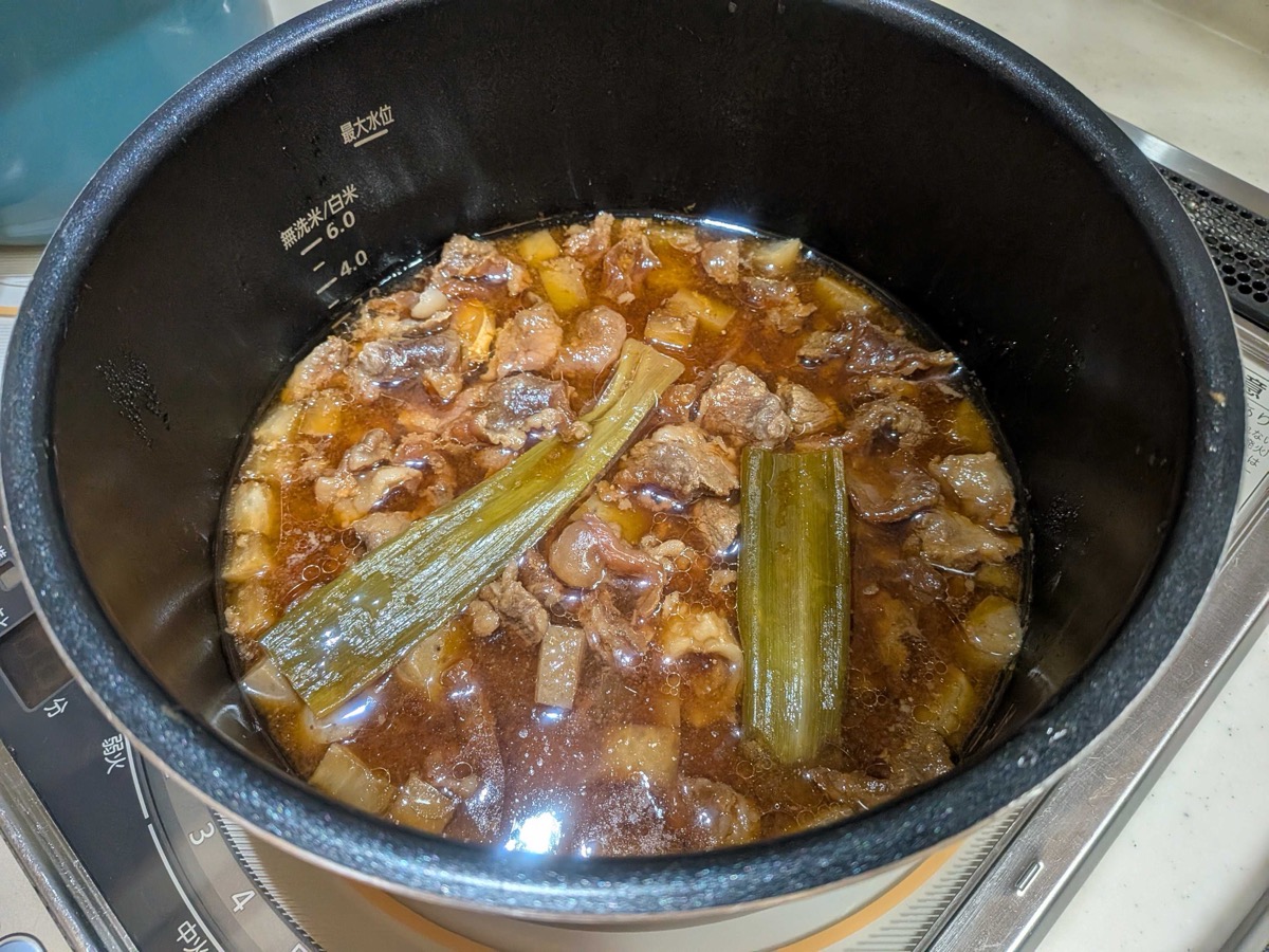 The finished gyusuji nikomi inside the electric pressure cooker — tender beef sinew, cubed daikon, and konnyaku swimming in a rich dark miso broth with the spent green scallion stalks floating on top