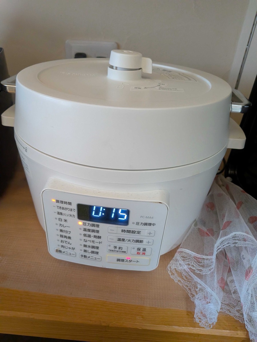 An Iris Ohyama electric pressure cooker (PC-MA4) on a wooden counter, its digital display showing 0:15 remaining while the beef sinew stew cooks under pressure