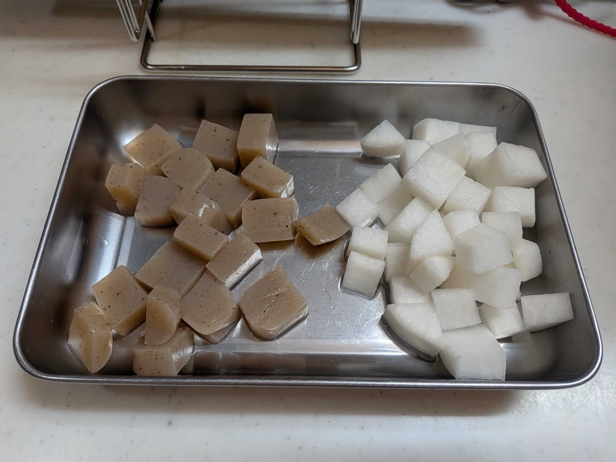 Cubed pre-treated konnyaku on the left and cubed white daikon on the right, arranged on a stainless steel tray — cut to matching 2 cm cubes for Japanese gyusuji nikomi