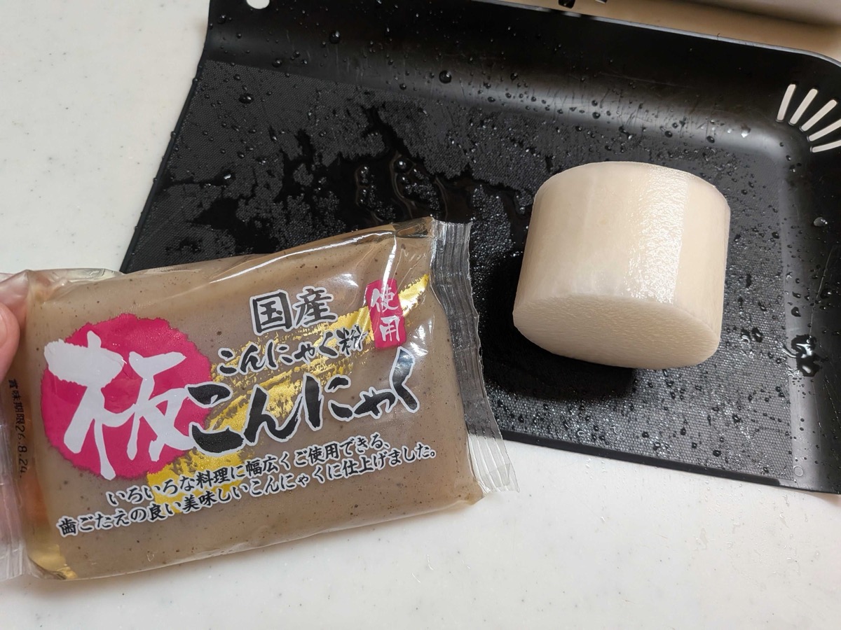 A package of Japanese ita-konnyaku (block konjac) and the pale brown block itself, unwrapped on a black tray — a traditional ingredient for gyusuji nikomi