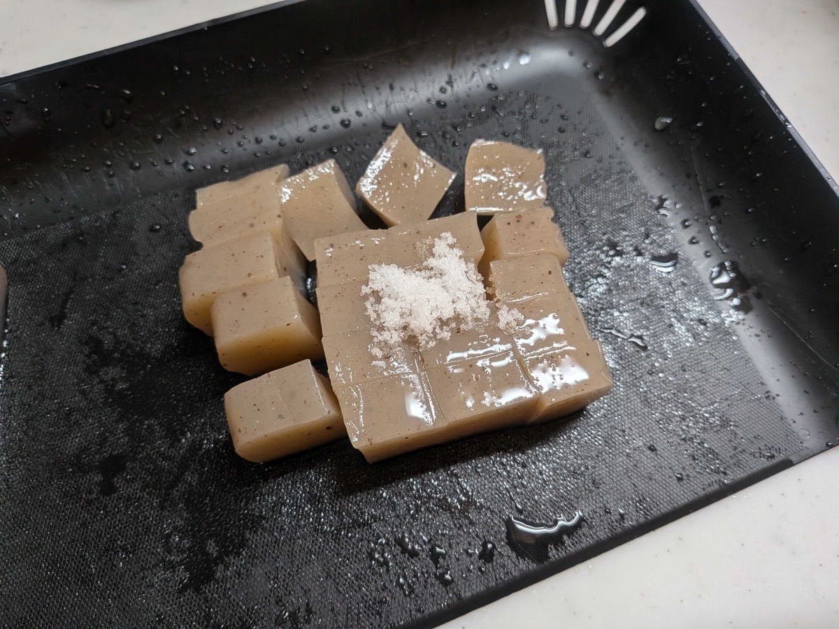 Cubed konnyaku with a pile of salt sprinkled on top, sitting on a black tray, ready to be salt-rubbed — a traditional Japanese preparation step