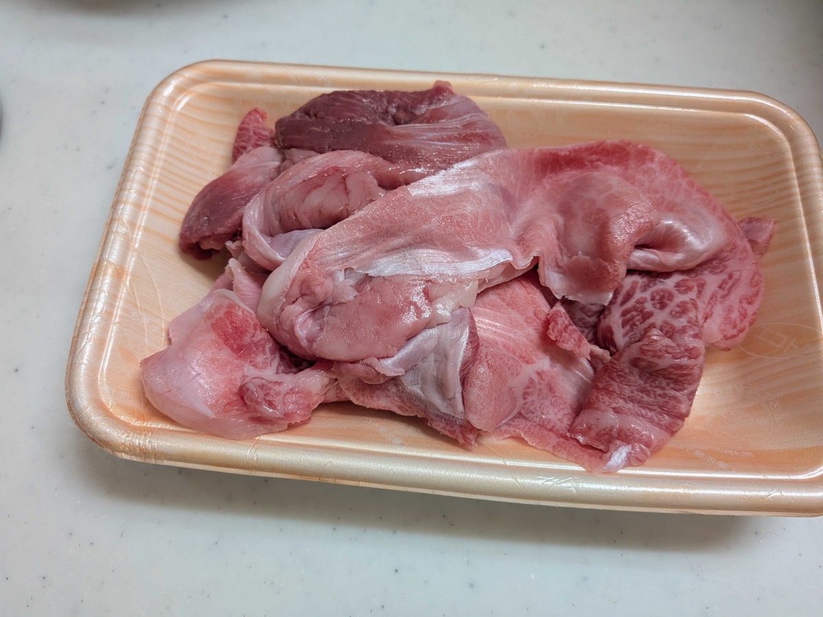 Raw beef sinew (gyusuji) on a styrofoam grocery tray — a mix of dark red meat, translucent connective tissue, and white fat, ready to be blanched for Japanese beef stew