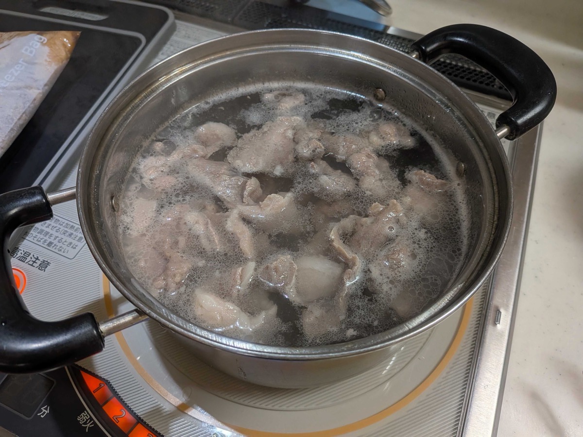 A pot of cloudy grey water with foam and scum rising to the surface as beef sinew boils — the impurities being drawn out for clean Japanese gyusuji nikomi broth