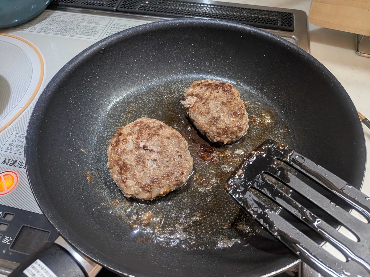 Two browned hamburg steaks in the pan being turned with a spatula