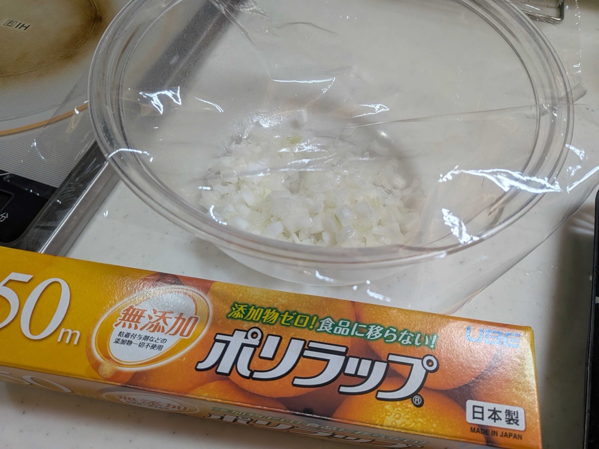 Chopped onion in a glass bowl ready to microwave, next to a box of plastic wrap