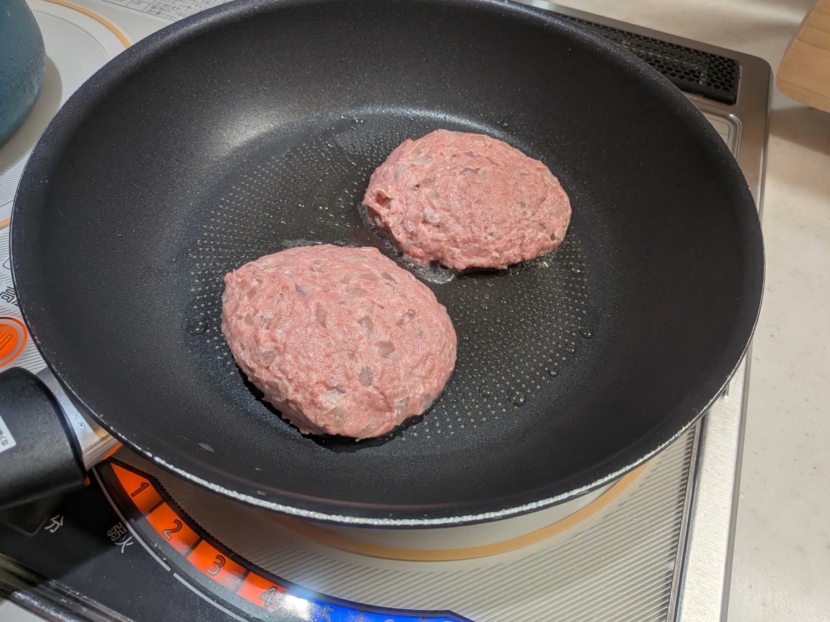 Two raw hamburg steak patties placed in a frying pan to sear