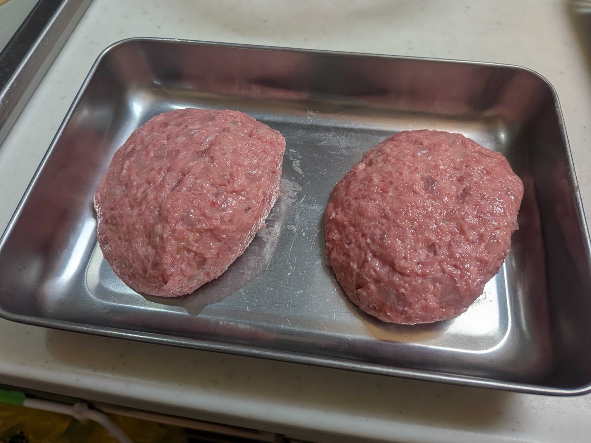 Two oval Japanese hamburg steak patties shaped and resting on a metal tray