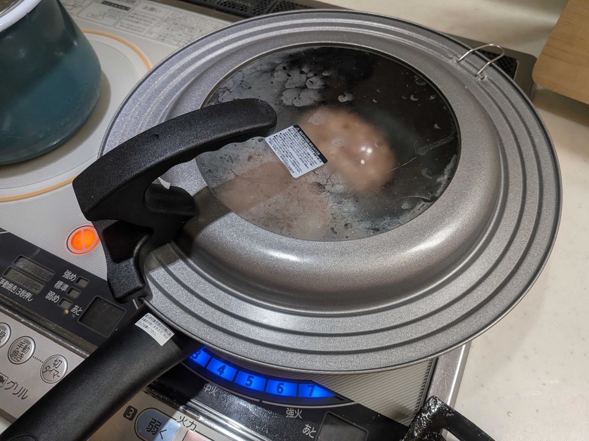 Hamburg steaks cooking under a glass lid in the frying pan with condensation