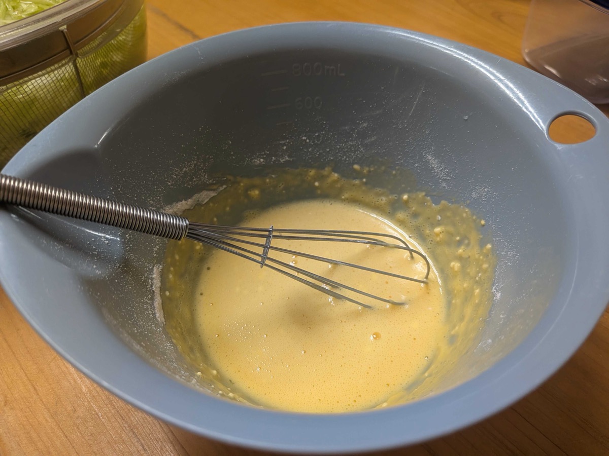 Smooth yellow batter made of egg, flour, and water whisked in a blue bowl