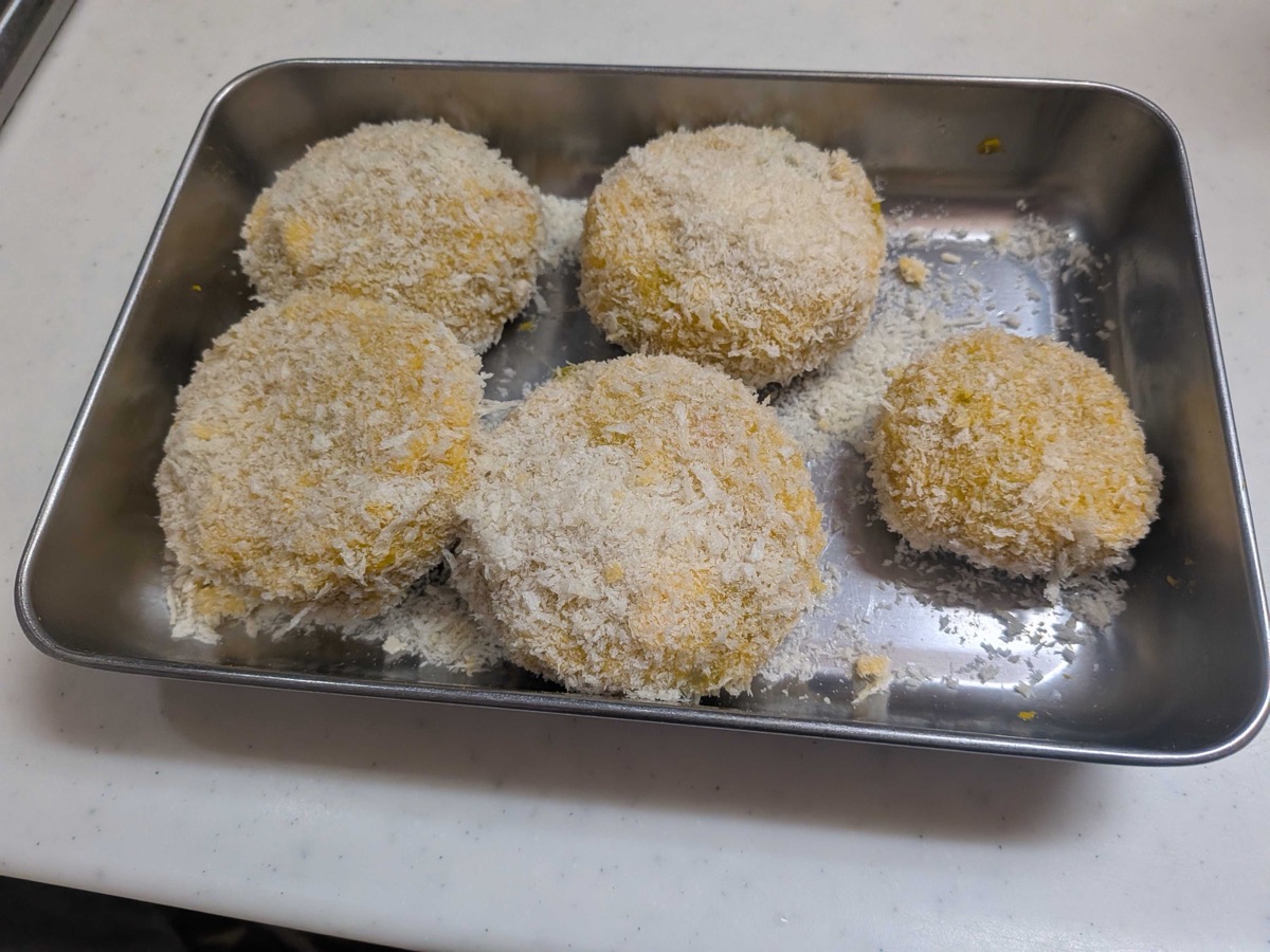 Five kabocha croquette patties fully coated in panko breadcrumbs on a metal tray