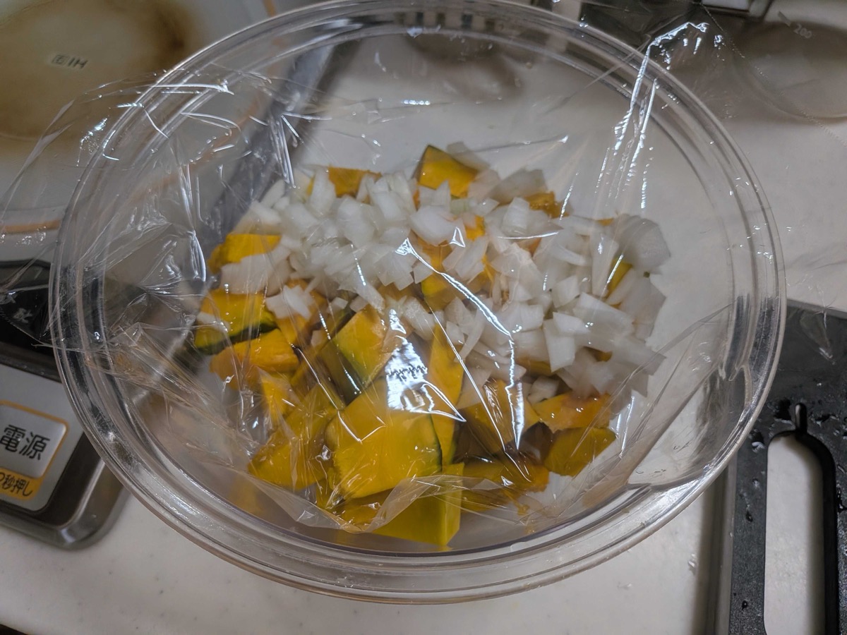 Glass bowl of kabocha pumpkin and onion covered with plastic wrap, ready to microwave