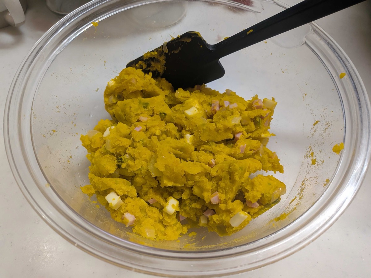 Mashed kabocha pumpkin filling mixed with diced ham and cubes of cheese in a glass bowl