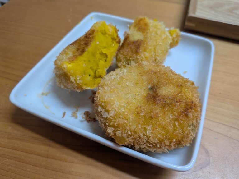 Golden panko-fried Japanese kabocha pumpkin croquettes on a white plate, one cut open to show the bright yellow creamy pumpkin and melted cheese inside