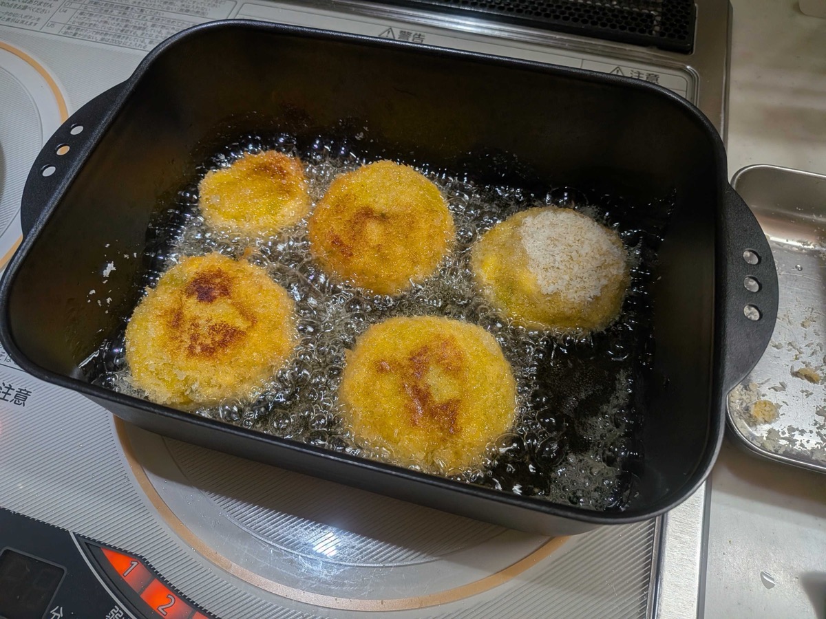 Kabocha pumpkin croquettes frying and turning golden brown in hot oil in a black pan