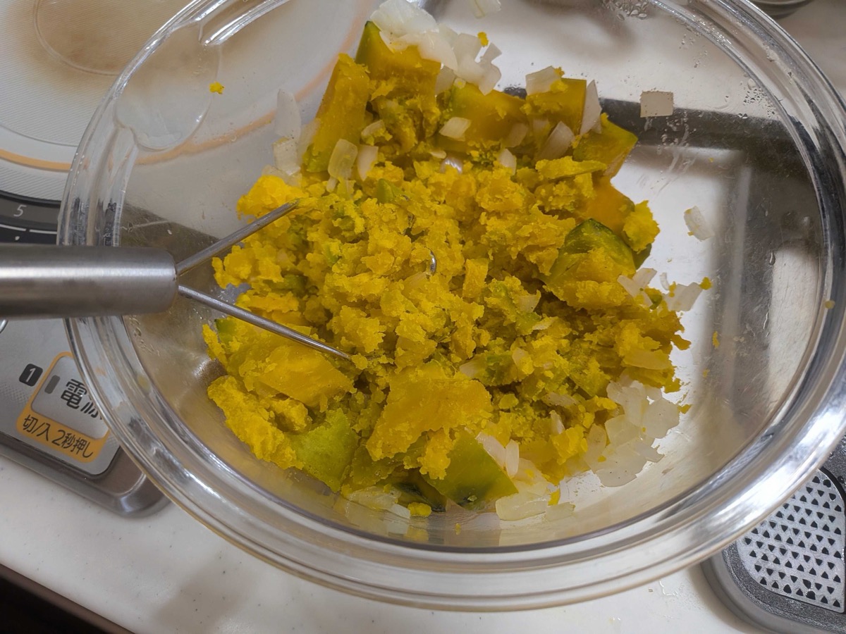 Steamed kabocha pumpkin and onion being mashed with a fork in a glass bowl