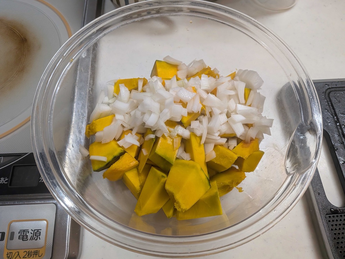 Chunks of raw kabocha pumpkin and finely chopped onion in a glass bowl, ready to be microwaved