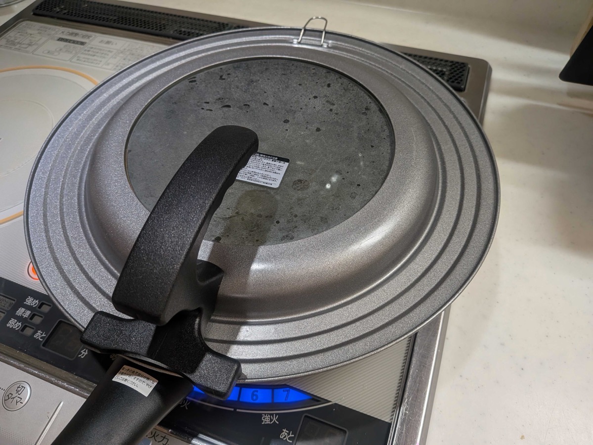 A pan lid placed on top of the frying pan on the IH cooktop, sealing in the steam as the kombu tsukudani simmers underneath during its first covered stage