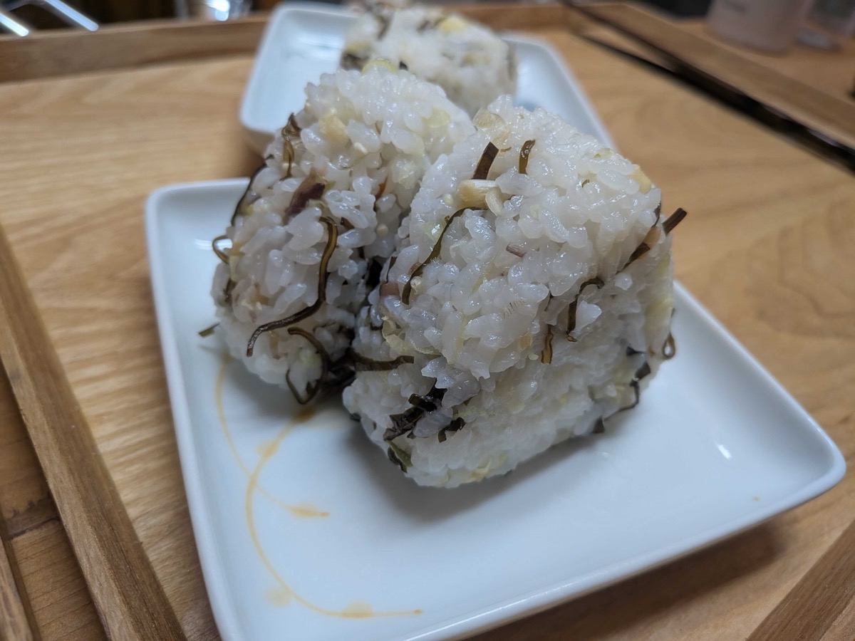 Three triangular myoga and shio kombu onigiri on a white plate