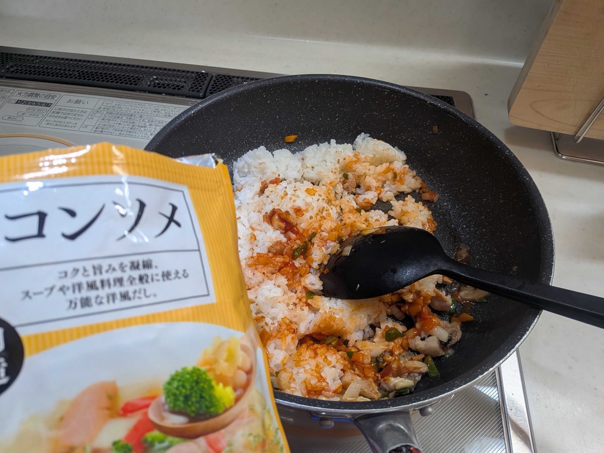 Consommé stock powder being sprinkled over the ketchup fried rice in the pan