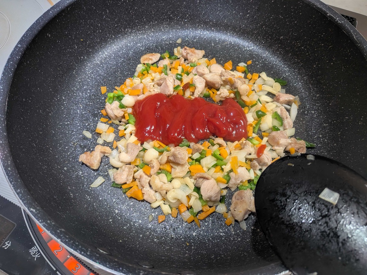 A generous spoonful of ketchup added to the pan of chicken and vegetables