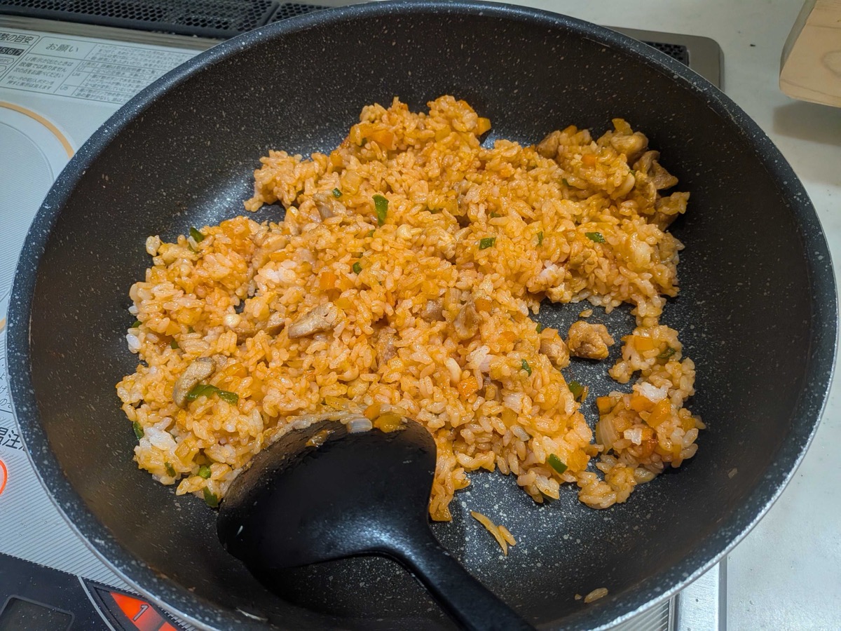 Finished ketchup chicken fried rice, evenly orange, in a frying pan