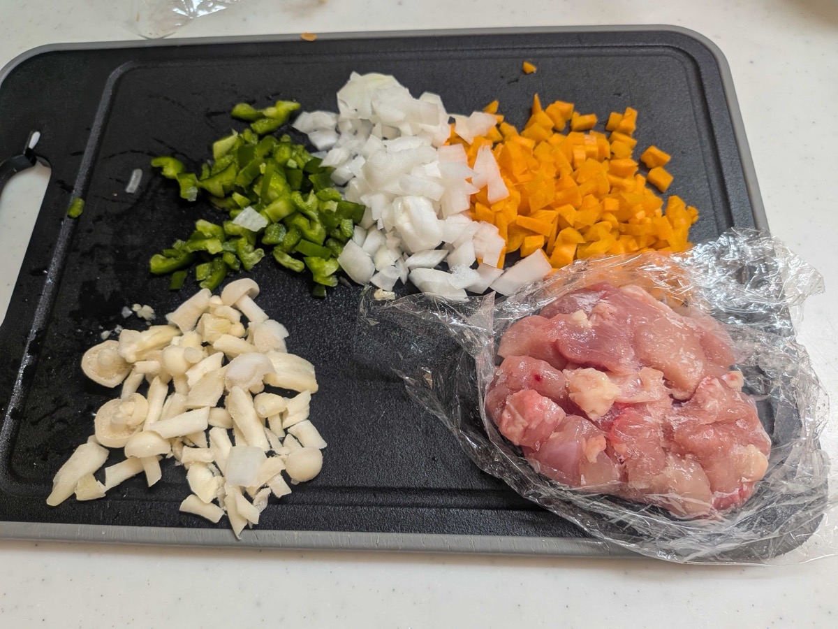 Finely chopped green pepper, onion, carrot, mushrooms and diced chicken thigh on a cutting board