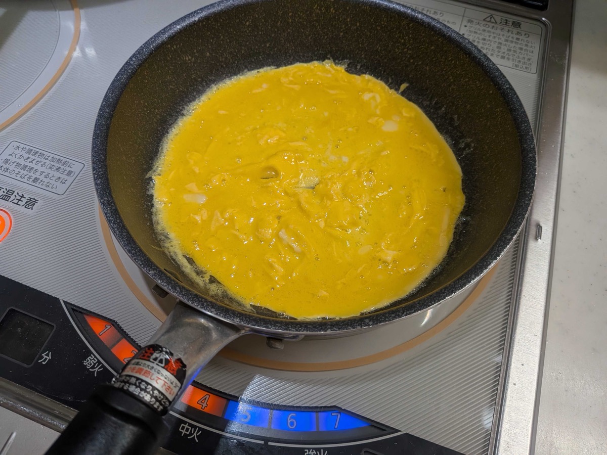 Beaten egg poured into the pan and spread out to cook into a thin omelette