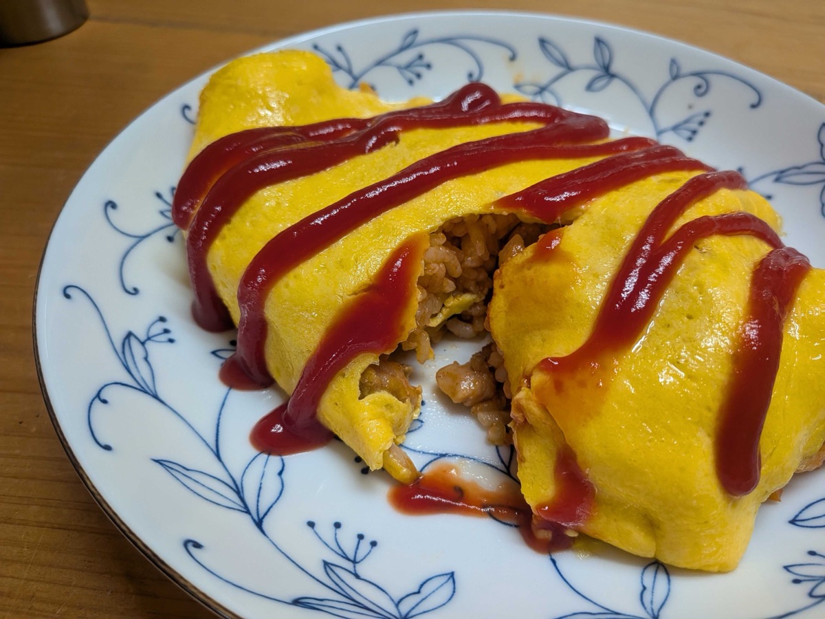 Omurice cut open to show the ketchup chicken rice inside the soft omelette, drizzled with ketchup