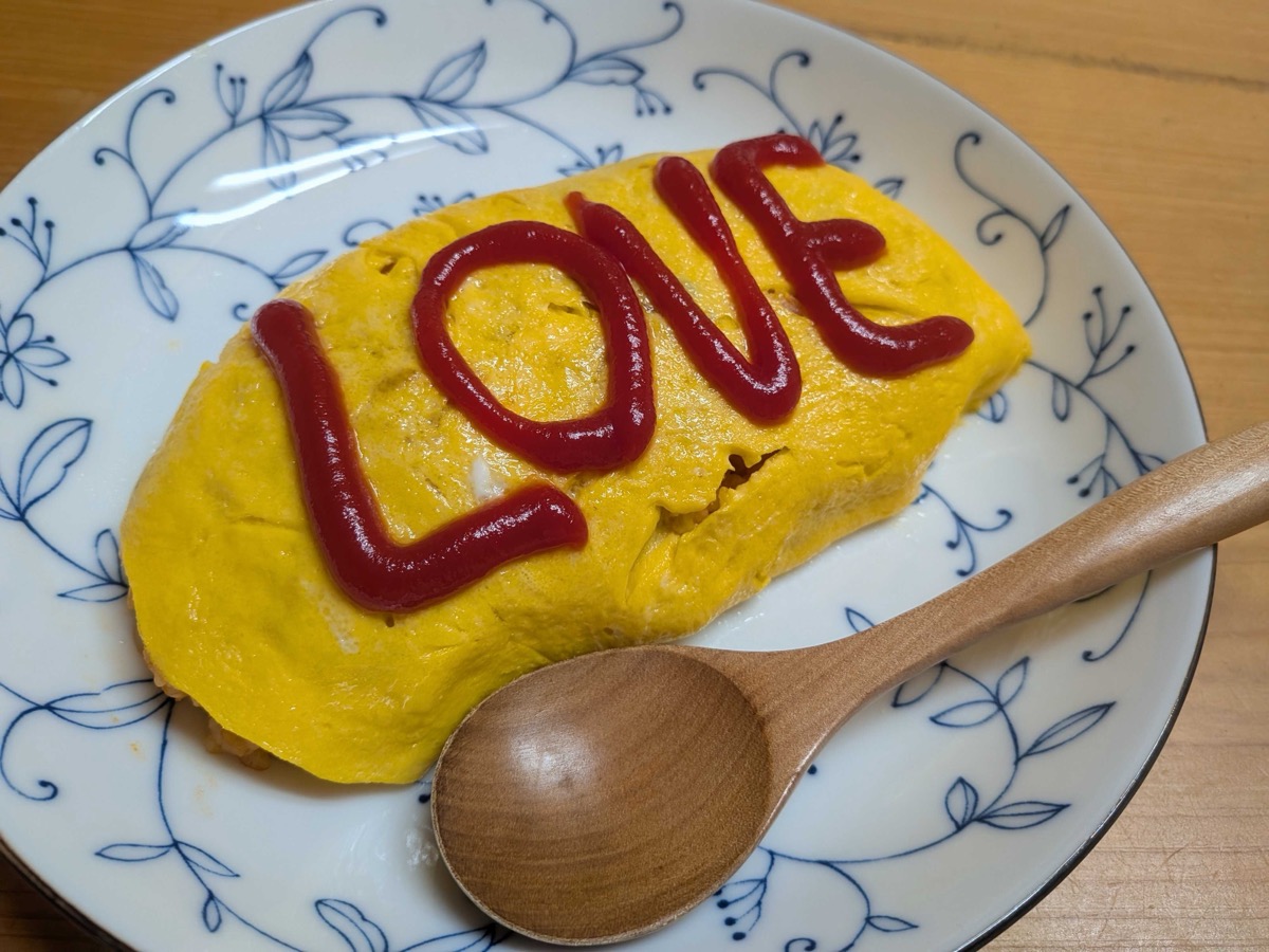 Japanese omurice on a blue-and-white plate with LOVE written in ketchup and a wooden spoon