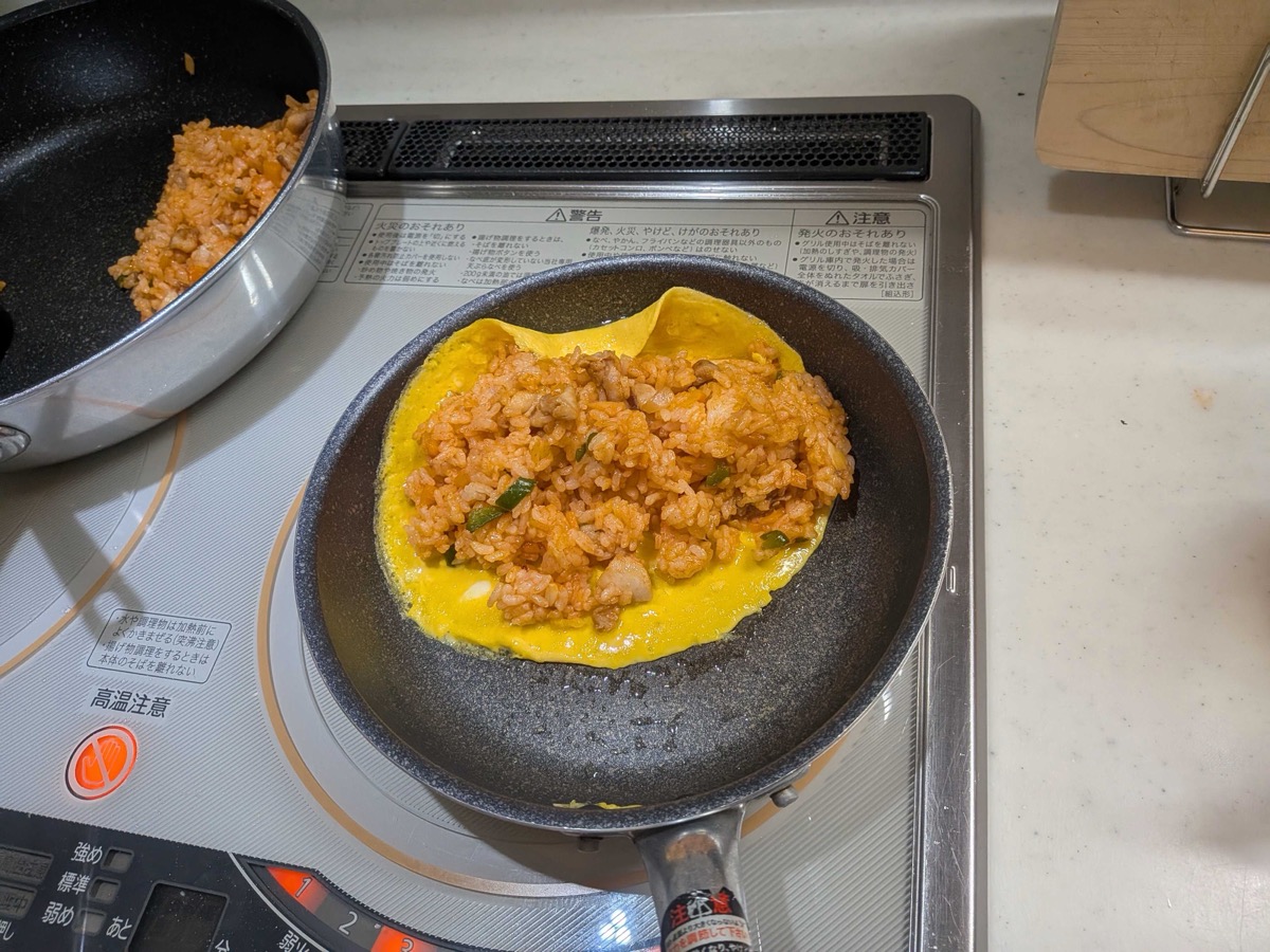 The omelette being folded over the mound of ketchup rice in the pan