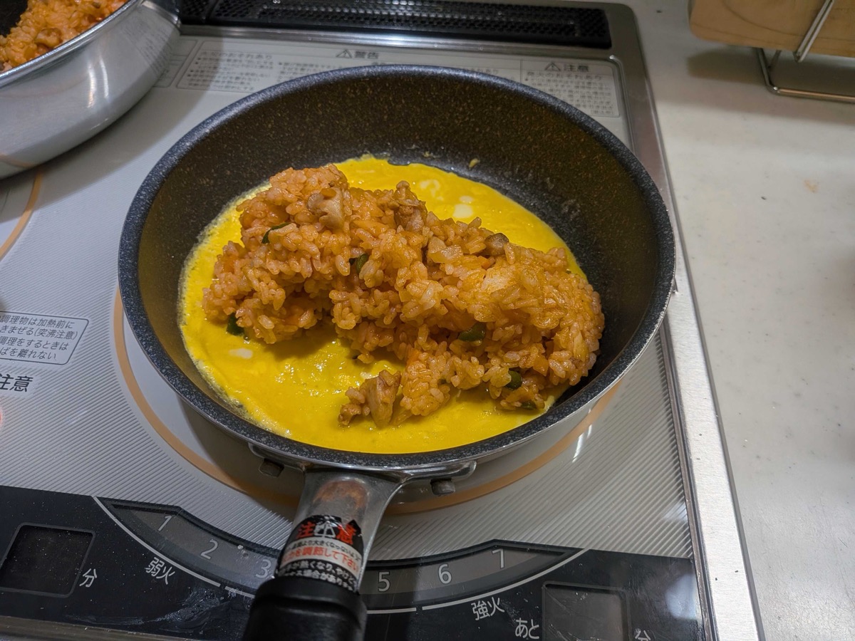 A mound of ketchup chicken rice placed on one side of the thin omelette in the pan