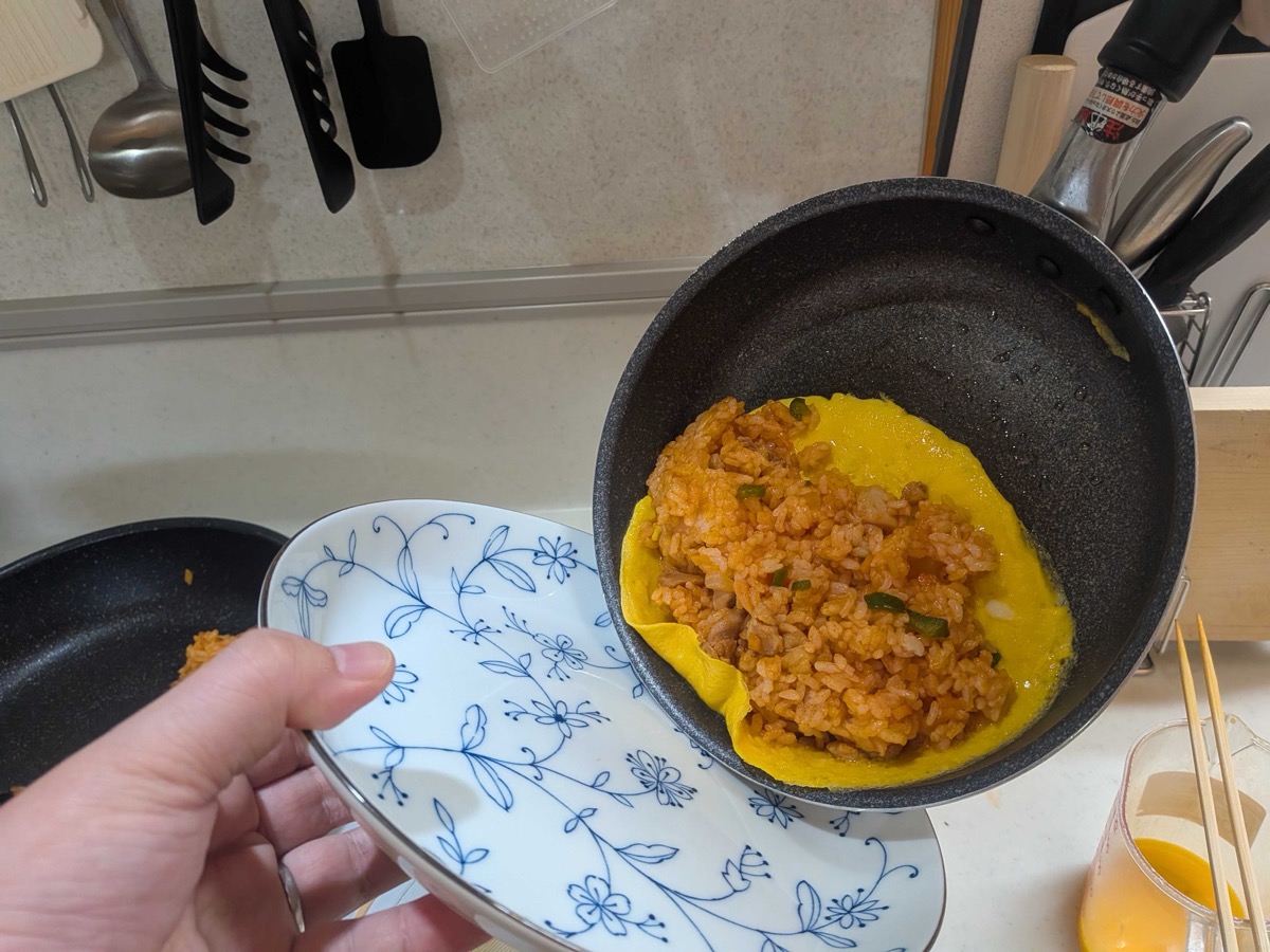 The folded omelette rice being slid out of the pan onto a blue-and-white plate